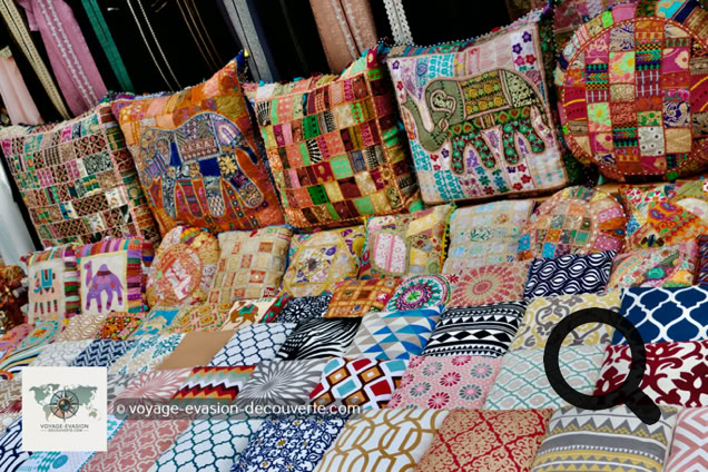 D'un côté, le souk du textile déploie ses galeries couvertes remplies de tissus colorés, de soies brodées, de pashminas et de cotons venus de toute l'Asie. Les étoffes pendent en cascades depuis les échoppes, créant un véritable arc-en-ciel permanent.